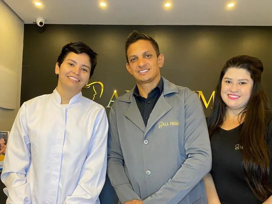 Três pessoas da equipe da All Prime na recepção, diante da logo dourada.