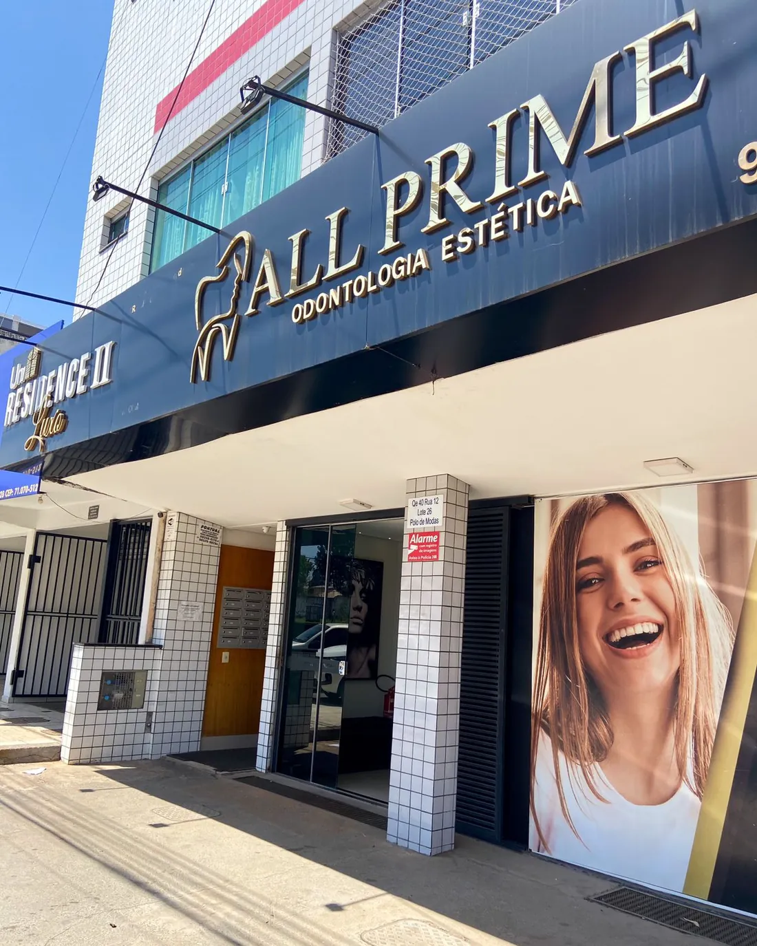 A fachada da All Prime num dia de sol, com o letreiro dourado ALL PRIME, Odontologia Estética, sobre a entrada de vidro.